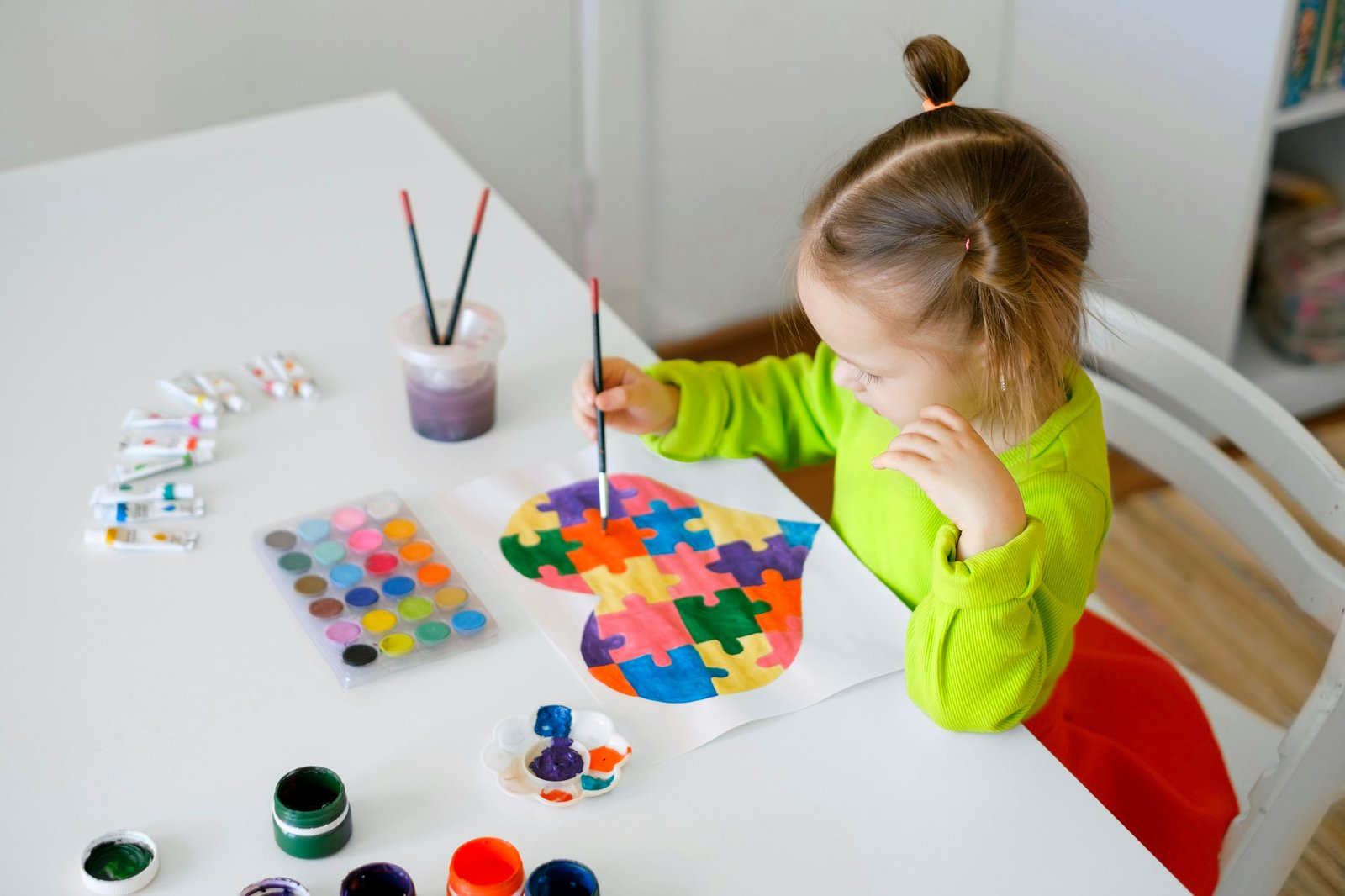 A girl draws drawing for autistic children with picture of heart from puzzles.